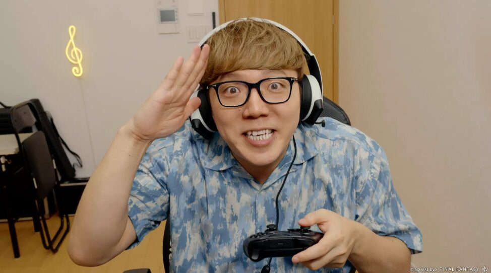 ゲーム機を片手に笑顔で敬礼するメガネの男性