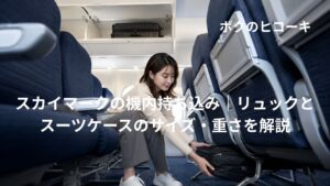 機内持ち込みスーツケースを頭上棚に入れ小型リュックを前席下へ収納する日本人旅行者